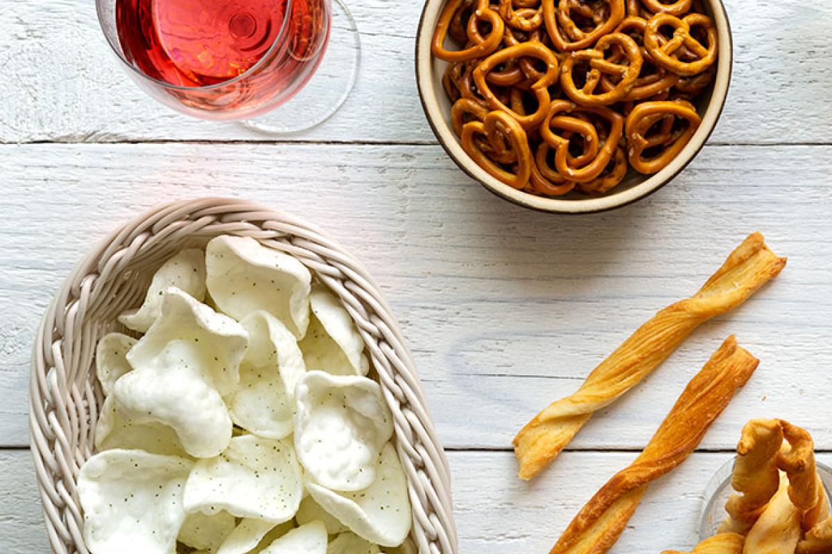 Glass of wine with chips and pretzels.